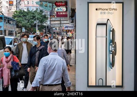 Pedestrians walk past an American multinational technology company Apple Iphone 13 Pro commercial advertisement in Hong Kong. Stock Photo