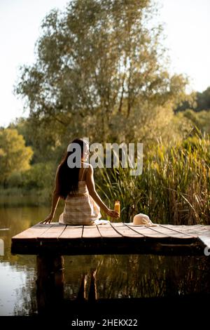 Young woman relaxing on the wooden pier at the calm lake on a hot summer day Stock Photo