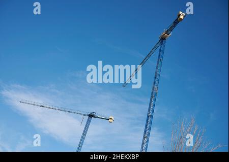 Construction cranes seen against a blue sky with clouds Stock Photo