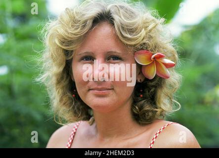 The beautiful face of a Seychelleois girl with a frangipani flower behind her ear in the Vallee de Mai National Park , on Praslin Island, the island of palms, in the Seychelle Islands, in the Indian Ocean off the east coast of Africa. Stock Photo