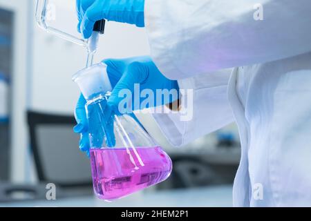 Close up scientist uses a titration method of analysis to study the chemical properties of the water sample. Scientist holding Erlenmeyer flask with pink solution Stock Photo