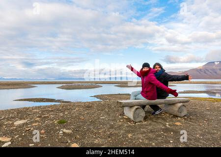 Back view portrait of young couple sitting on a bench, young couple on vacation - svalbard, arctic landscape Stock Photo