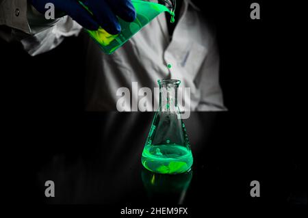 A research scientist experimenting with a green fluorescent droplets in a glass conical flask in dark biomedical laboratory for health care medicine d Stock Photo