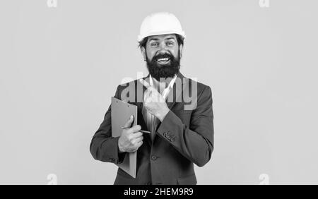 man with beard and moustache in helmet look as businessman on construction site, boss pointing finger Stock Photo