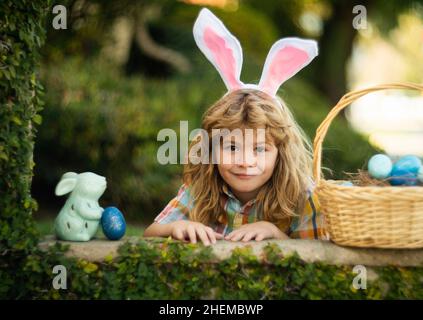 Kid boy hunt egg in easters basket on Easter day outdoor. Kids Easter bunny hunting eggs, wear rabbit ears. Spring family holiday. Stock Photo