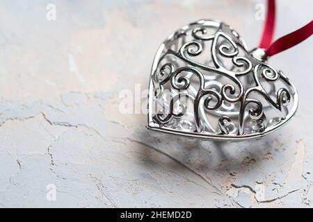 Saint Valentine day greeting card, beautiful silver heart with red ribbon on grey textured background Stock Photo