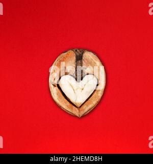 Funny Minimalistic Saint Valentine Day concept, open half of walnut with core looking like heart or owl face on red Stock Photo
