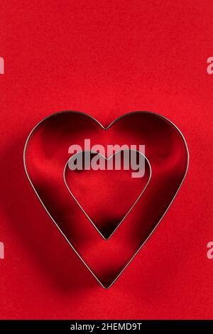 Saint Valentine day minimalistic greeting card, heart-shaped cookie cutters on red background with beautiful shadows, flat lay Stock Photo