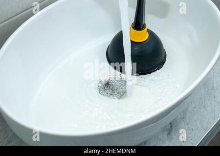 Cleaning sink with plunger in bathroom. Concept of plumbing problem and drain clogs. Stock Photo