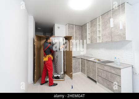 Young Male Mover Placing Steel Refrigerator In Kitchen Stock Photo