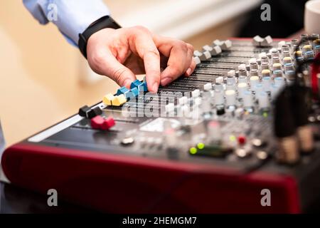 a professional audio engineer uses an audio mixer control panel console to create a music track in a recording studio. the DJ switches slides and work Stock Photo