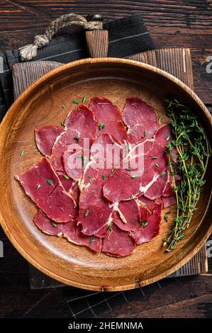 Pastrami slices, dried beef meat with herbs in wooden plate. Wooden background. Top view Stock Photo