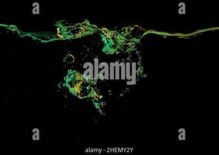 Clear water surface with ripple and bubbles in green and yellow light on a black nature background Stock Photo