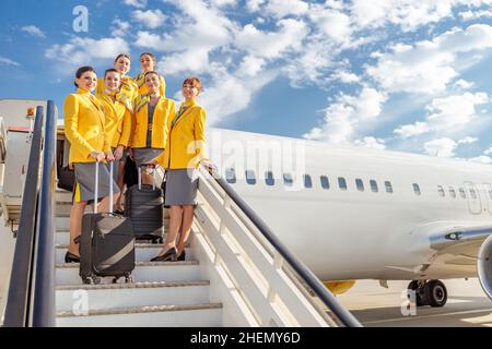 Cheerful women flight attendants holding travel bags and smiling while standing on plane boarding stairs Stock Photo