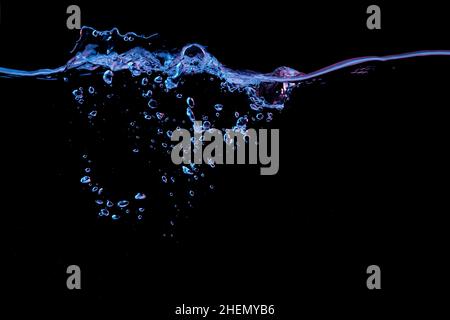 Clear water surface with ripple and bubbles in red and blue light on a black nature background Stock Photo