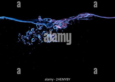 Clear water surface with ripple and bubbles in red and blue light on a black nature background Stock Photo