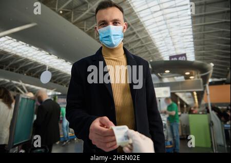 Handsome young man in a protective medical mask receives a QR code after being tested before departure at the international airport. Safe flight and t Stock Photo