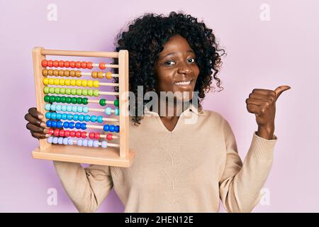Young african american woman holding traditional abacus pointing thumb up to the side smiling happy with open mouth Stock Photo