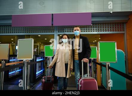 Young couple of business partners in protective medical masks, standing with suitcases at check-in counter, waiting for check-in, passing customs and Stock Photo