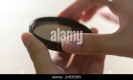 Close up of polarizing lens filter in girls hands isolated on white background. Woman turning into the both sides mechanism of lens filter. Stock Photo