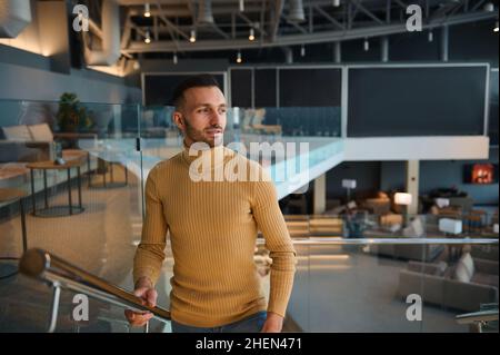 Handsome attractive Caucasian confident man, businessman on business trip climbs the stairs in waiting room of departure terminal at international air Stock Photo
