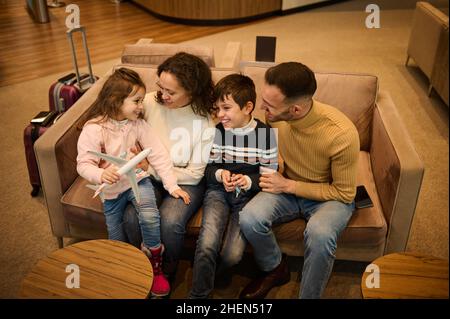 Happy family. Parents admiring their kids playing with toy planes, discussing the upcoming air trip, resting in the VIP lounge of the airport departur Stock Photo