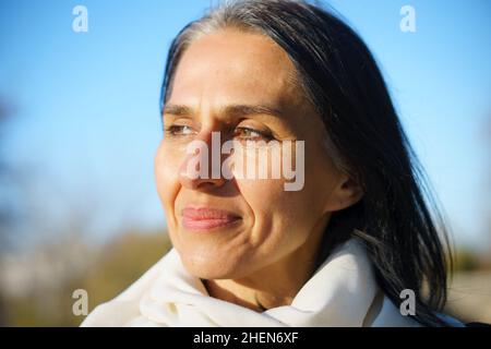 Profile side view portrait of attractive cheerful dreamy grey-haired middle-aged woman relaxing outdoors during sunny day Stock Photo