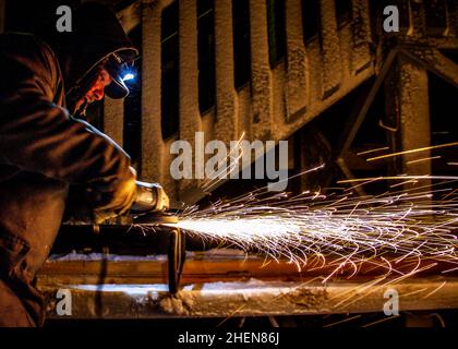 A man grinding metal in the cold and in the dark with winter gear on Stock Photo