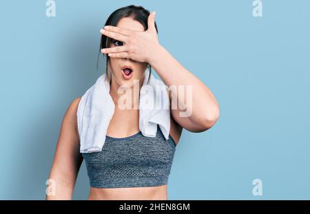 Young hispanic girl wearing sportswear and towel peeking in shock covering face and eyes with hand, looking through fingers with embarrassed expressio Stock Photo