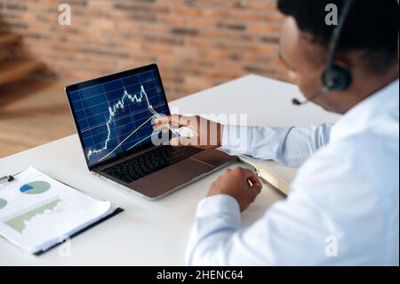 Smart focused african american broker investor, uses laptop to analyze financial cryptocurrency market, invest in e-currency, buy or sell crypto coins, analyze financial data, develop strategy Stock Photo