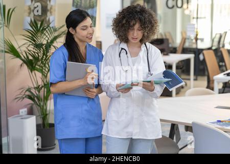 Concentrated female doctor with curly hair talking with a nurse and looking at paperwork. Stock Photo