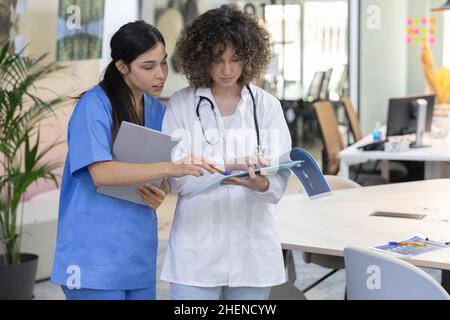 Concentrated female doctor with curly hair talking with a nurse and looking at paperwork. Stock Photo