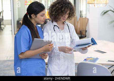 Concentrated female doctor with curly hair talking with a nurse and looking at paperwork. Stock Photo