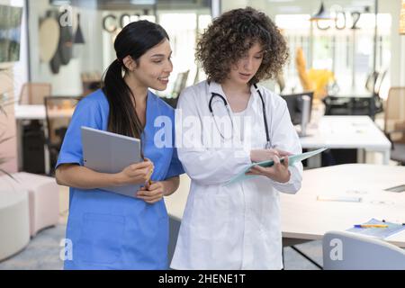 Concentrated female doctor with curly hair talking with a nurse and looking at paperwork. Stock Photo