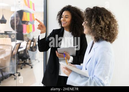 Multicultural coworkers using white board and doing brainstorming together. Co-working concept Stock Photo