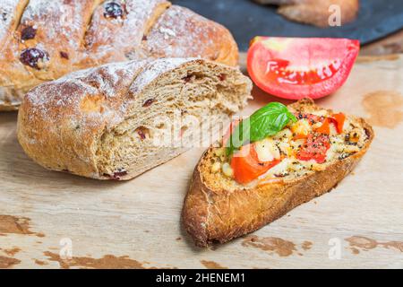 Italian bruschetta with roasted tomatoes, mozzarella cheese and herbs on a cutting board Stock Photo