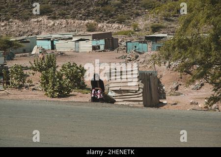 Djibouti, Djibouti - May 21, 2021: A Djiboutian woman sitting by the roadside under the sun. Editorial shot in Djibouti Stock Photo