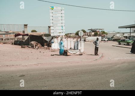 Djibouti, Djibouti - May 21, 2021: A Djiboutian man and two Djiboutian woman in local dress waiting by the street in Djibouti. Editorial shot in Djibo Stock Photo