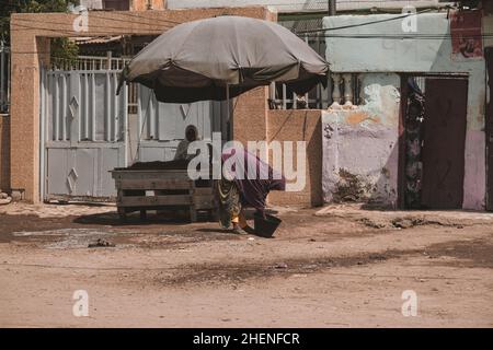 Djibouti, Djibouti - May 21, 2021: Two Djiboutian saler woman sitting in shade of umbrella in Djibouti. Editorial shot in Djibouti Stock Photo