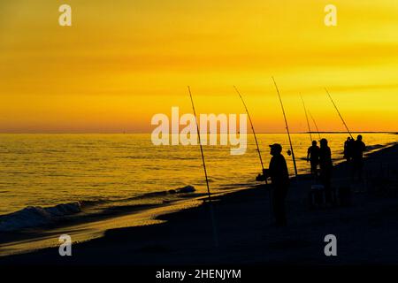 silhouette of people fishing at sunset on Dauphin Island in Alabama. Stock Photo