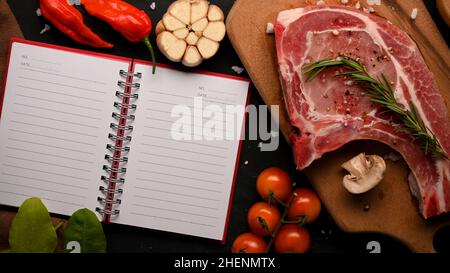 Raw pork chop steak with special seasoning on wooden board and an open notebook with blank pages for display your text. Food recipe book. top view Stock Photo