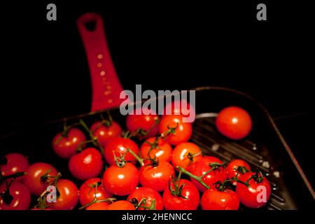 Ripe cherry tomatoes on a red-handled griddle. Stock Photo