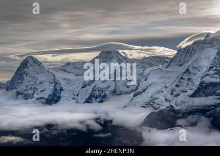 View of the famous peaks Jungfrau, Mönch, and Eiger from the mountain Schilthorn in the Swiss Alps Switzerland at sunrise with clouds and fresh snow. Stock Photo