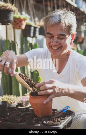 senior asian man smiling with happiness while planting at home garden Stock Photo