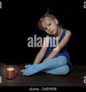 beautiful little girl in a blue dress is sad by a burning candle Stock Photo