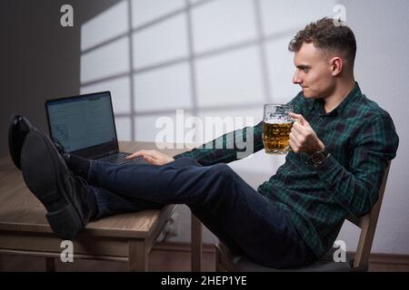 Young business man working at his laptop while drinking a non alcoholic beer from a mug Stock Photo