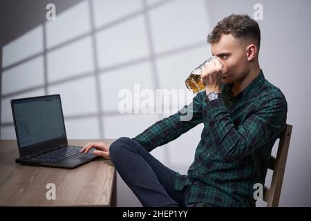 Young business man working at his laptop while drinking a non alcoholic beer from a mug Stock Photo