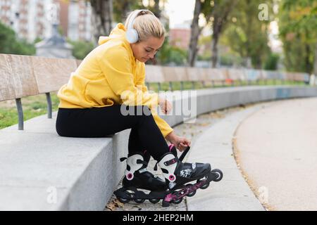 Woman listening to music while tying the inline skates in a city park Stock Photo
