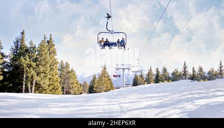 Group of skiers enjoying on the ski lift at the ski resort having fun. Winter mountains panorama with ski slopes and ski chairlift. Stock Photo