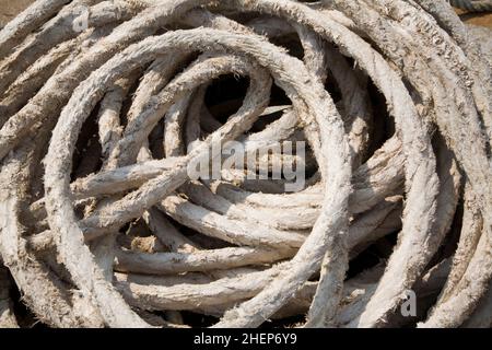 A weathered coil of heavy duty rope and the quay at Weymouth harbour, Dorset England. Used for general marine applications such as tying up vessels Stock Photo